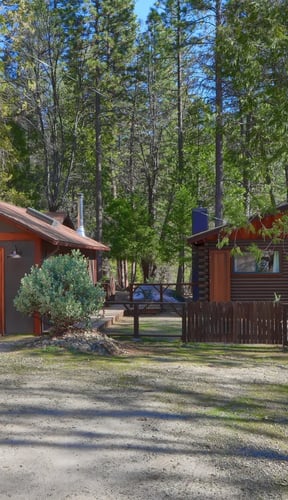 Classic log cabin with red-trim garage and pine forest backdrop