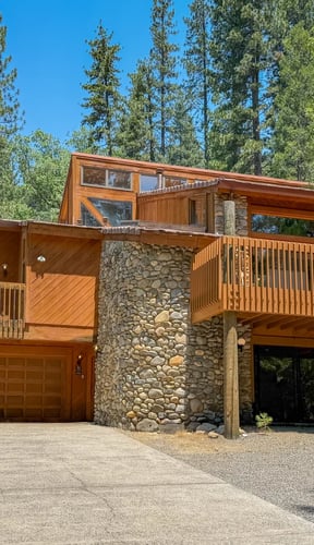 Two-story wood and stone cabin with wraparound decks under a clear blue sky