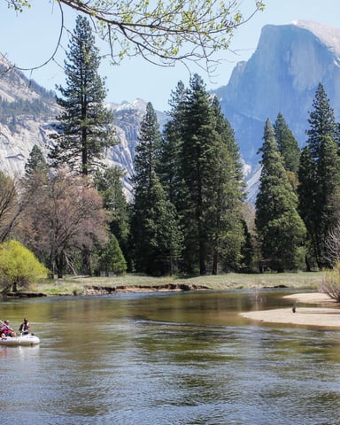 Two people rafting on the Merced River with Half Dome visible in the background