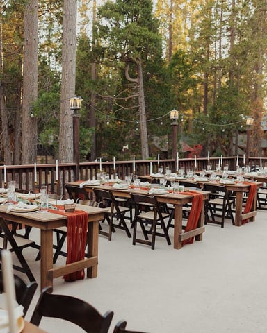 Outdoor event deck set for dinner with string lights and pine trees at dusk