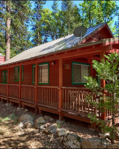 Red cabin with metal roof and wraparound porch surrounded by tall pine trees and boulders