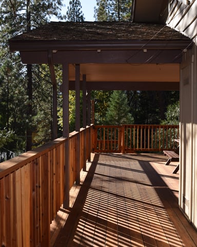 Wooden deck with metal railing extending from modern house, surrounded by tall pine trees