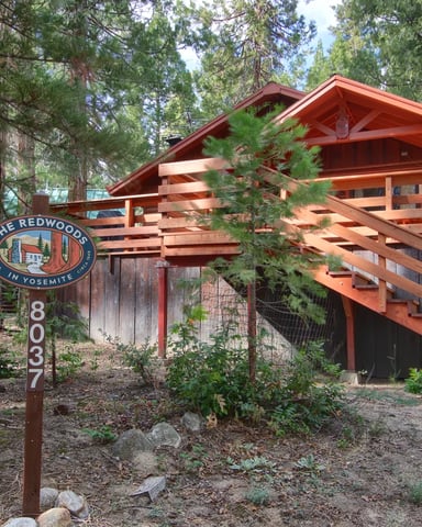 Warm redwood cabin with The Redwoods in Yosemite sign and open staircase among tall pines
