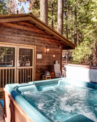 Bubbling hot tub on a wood deck beside a cedar cabin in the pines — Cedar Chalet