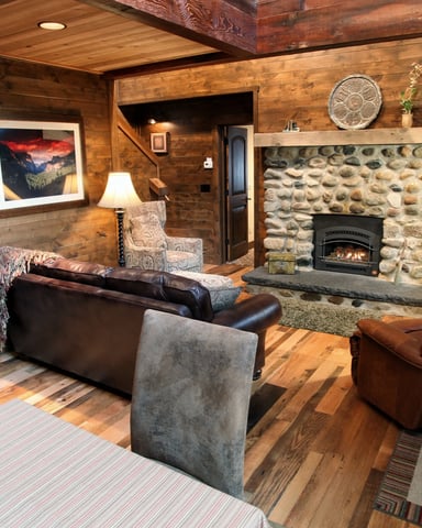 Rustic wood cabin living room with stone fireplace, leather seating, and mountain landscape artwork