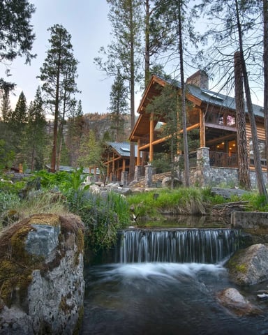 Log cabin above a waterfall in a forested canyon at dusk