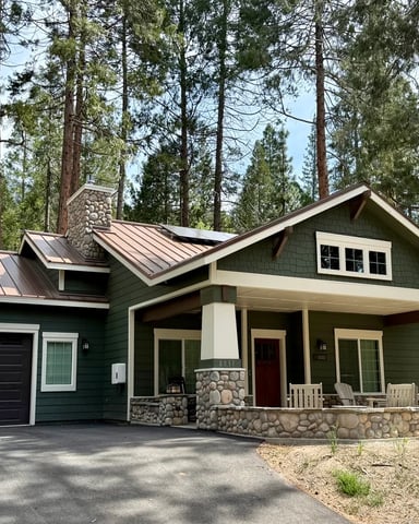 Green craftsman cabin with stone columns, covered porch, and copper metal roof — Black Bear Bungalow