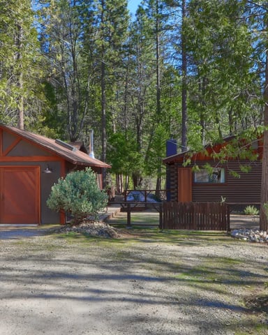 Dark log cabin with red garage and gravel driveway surrounded by pines — Camp Duke
