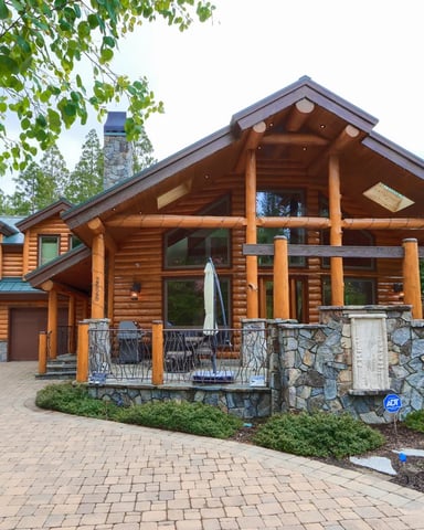 Grand log cabin with stone terrace, covered porch, and tall pines — The Lodge