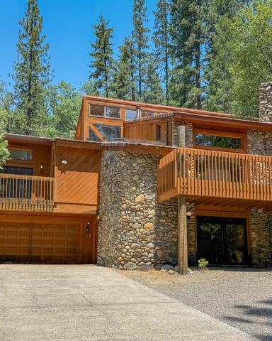 Cedar and river-stone home with wraparound decks and garage, surrounded by tall pines — Summit House