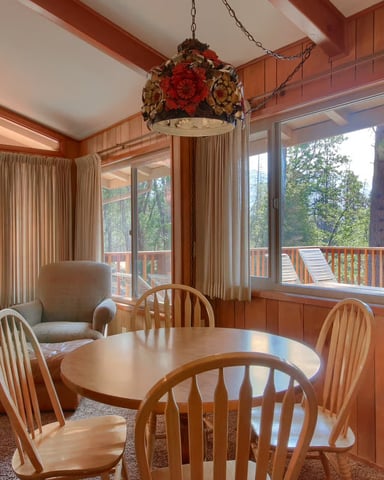Wide cabin with stone chimney and wraparound deck in a sunny pine forest — Yosemite Mountain Lodge