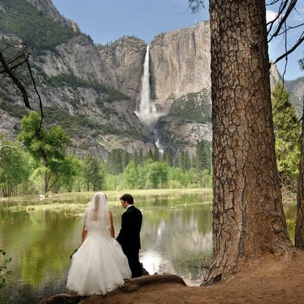 Wedding couple by the Merced River with Yosemite Falls in background