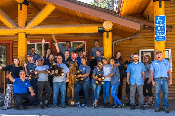 Group of staff and community members gathered under a wooden lodge structure