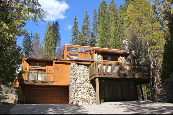 Modern mountain home with orange wood siding and stone chimney surrounded by tall pine trees